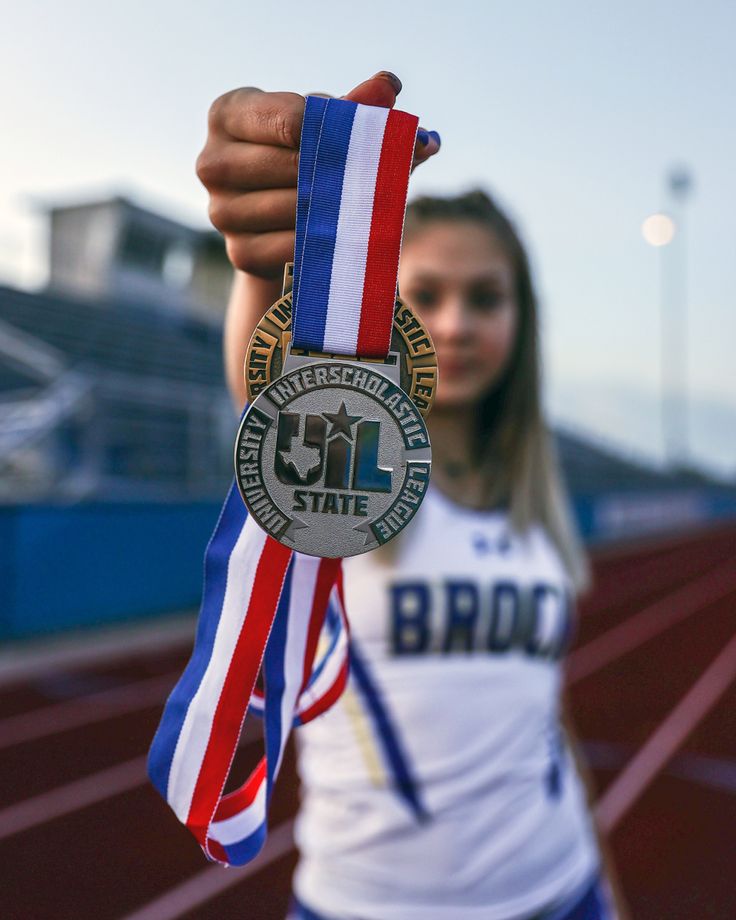 Female athlete holding a UIL State medal in front of track field